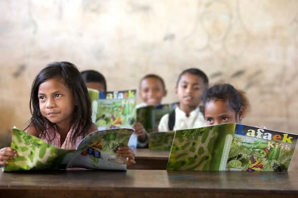 School children in Timor-Leste read their copies of CARE's educational magazine 'Lafaek', which is the only publication in the country that uses the national language Tetun. Image: Jane Dempster/CARE.